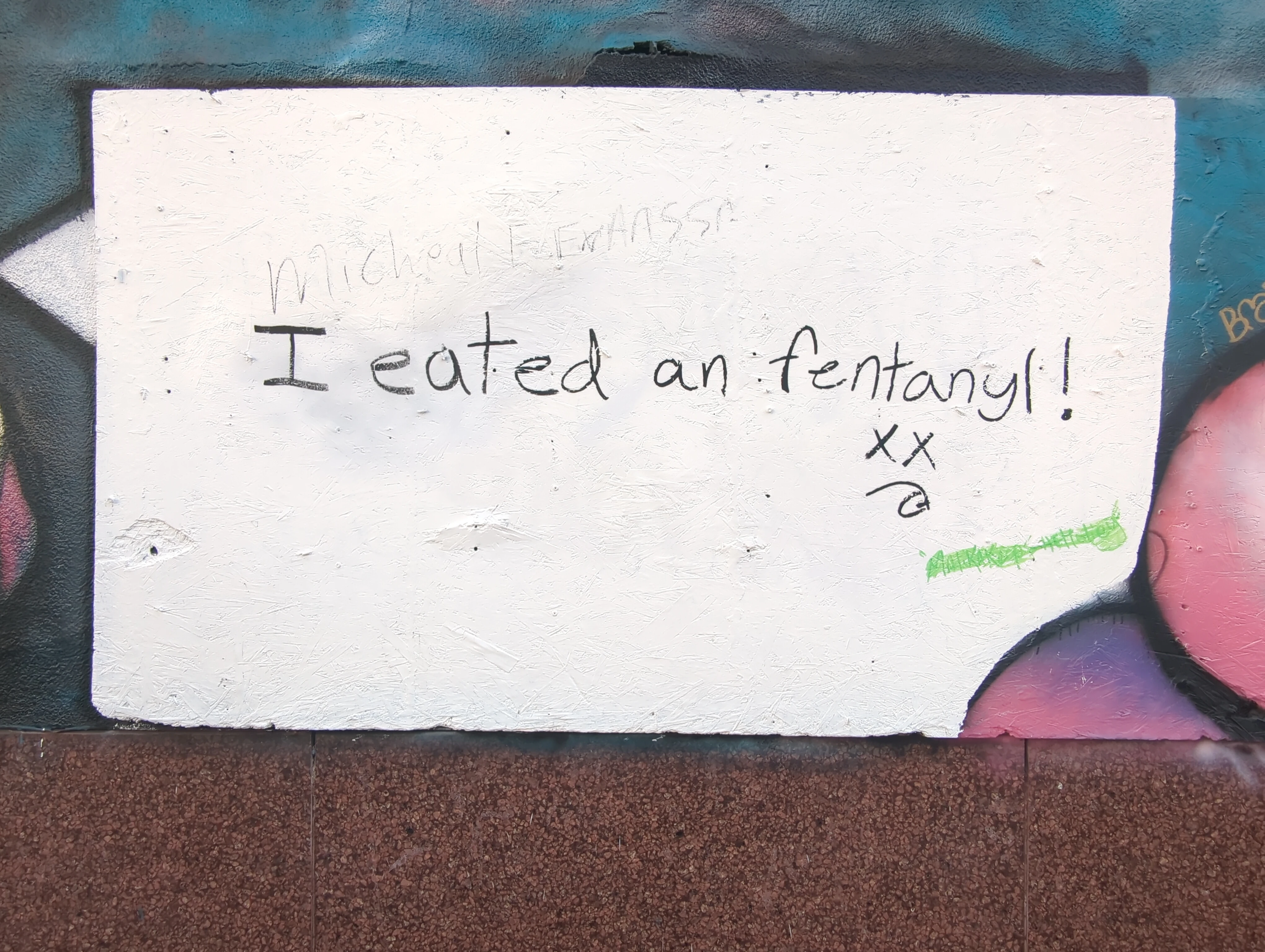 Street graffiti with text reading "I eated an fentanyl!" followed by a simplicistc depection of a face with Xs for eyes and a stuck out tounge.